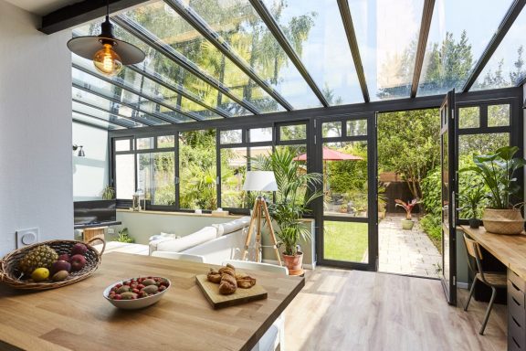Verrière moderne avec un espace lumineux, plantes et accès à un jardin verdoyant.